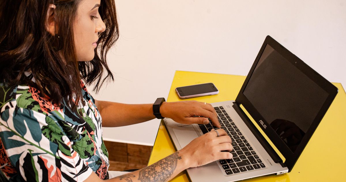 Mulher trabalhando em um laptop sobre uma mesa amarela