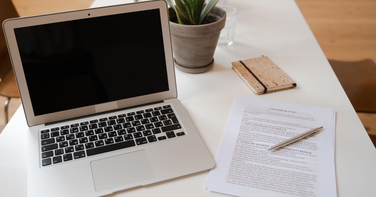 Mesa de escritório com notebook, planta e um documento de contrato
