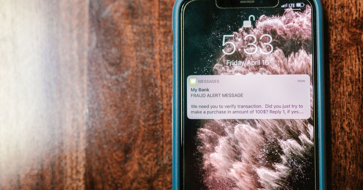 Celular sobre uma mesa de madeira exibindo uma notificação de alerta de fraude