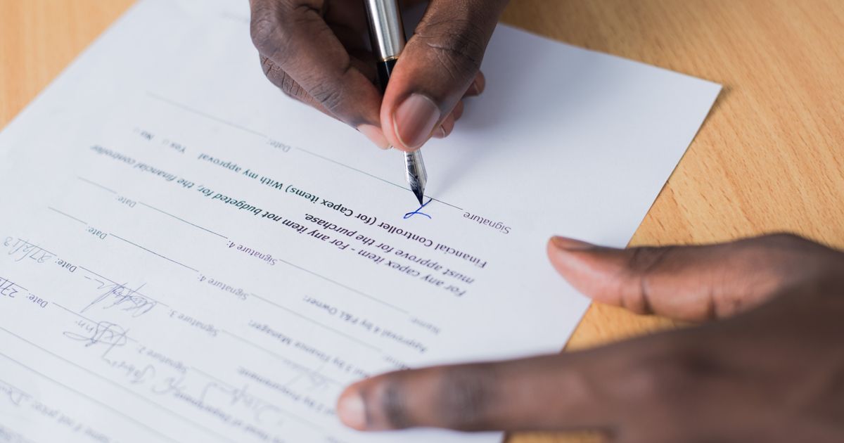 Mão de uma pessoa assinando um contrato com caneta sobre uma mesa